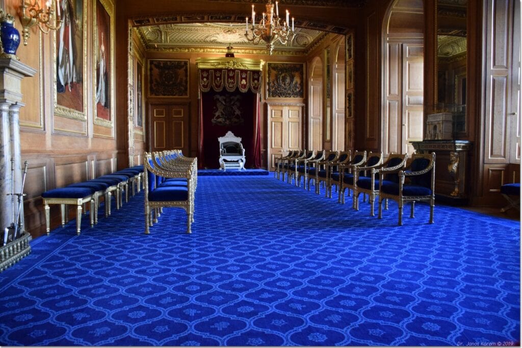 Windsor Castle 13 A long room with a deep blue patterned carpet, a canopied throne at the far end and gilt chairs ranged along both walls