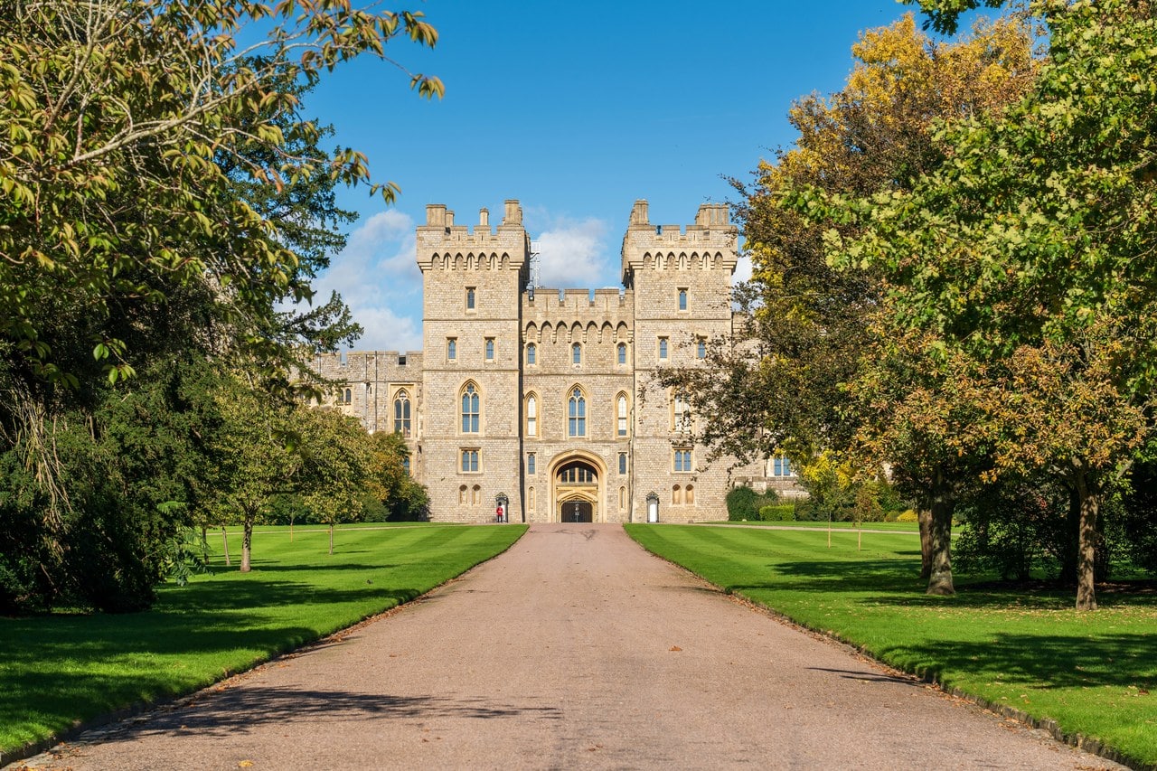 A twin-turreted stone gateway at the end of a straight drive, framed by trees whose leaves are turning yellow A twin-turreted stone gateway at the end of a straight drive, framed by trees whose leaves are turning yellow