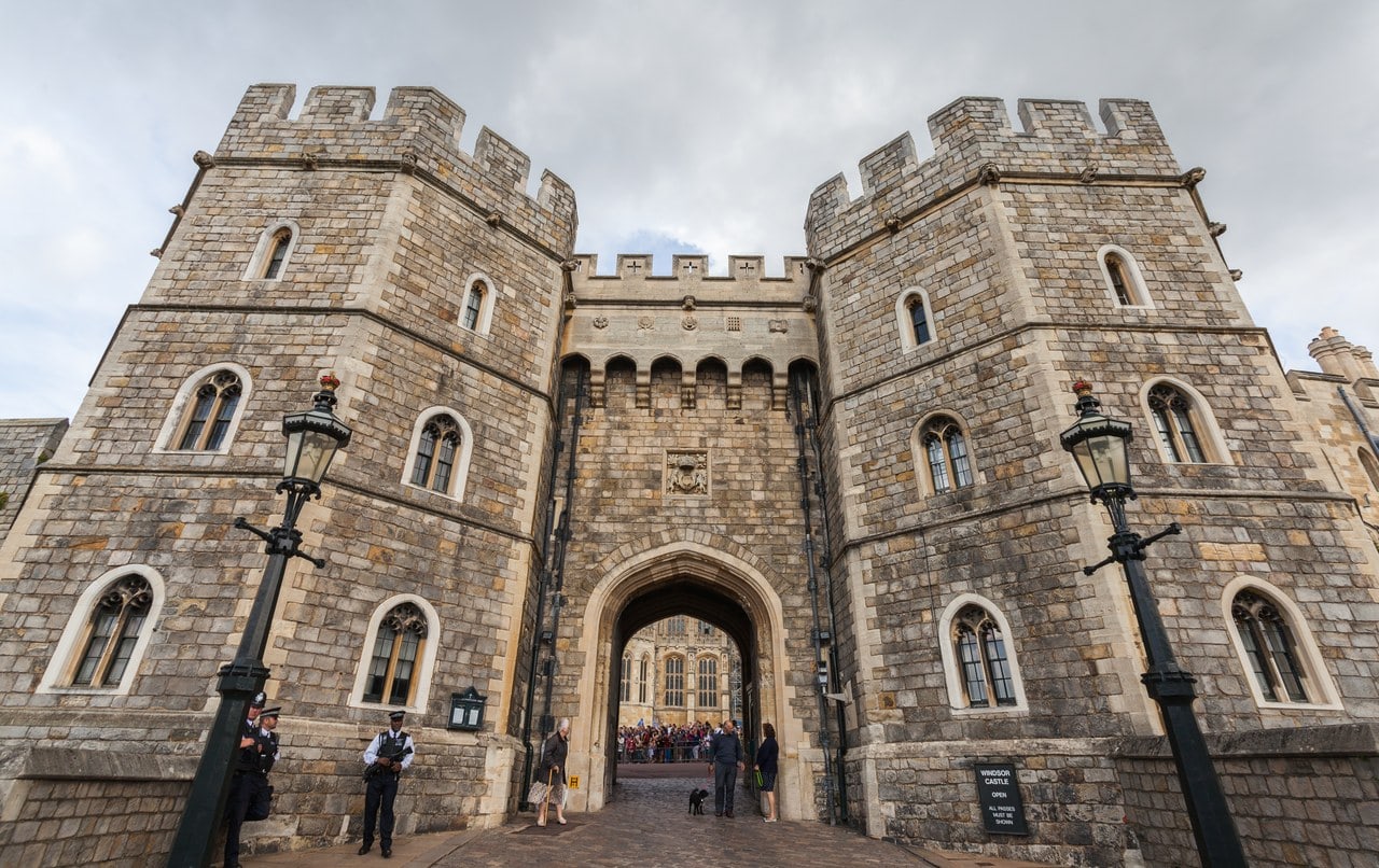 A twin-towered Tudor gatehouse with semi-octagonal fronts and a pointed arch, a carved coat of arms above it, seen from the street A twin-towered Tudor gatehouse with semi-octagonal fronts and a pointed arch, a carved coat of arms above it, seen from the street
