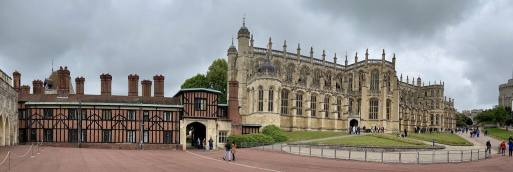 Windsor Castle 9 A curving range of timber-framed houses with tall brick chimneys, standing beside the pinnacled west end of a Gothic chapel