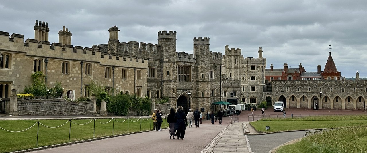 A wide view along a broad paved ward between battlemented ranges, with visitors walking and an arcaded stone wall closing one side A wide view along a broad paved ward between battlemented ranges, with visitors walking and an arcaded stone wall closing one side
