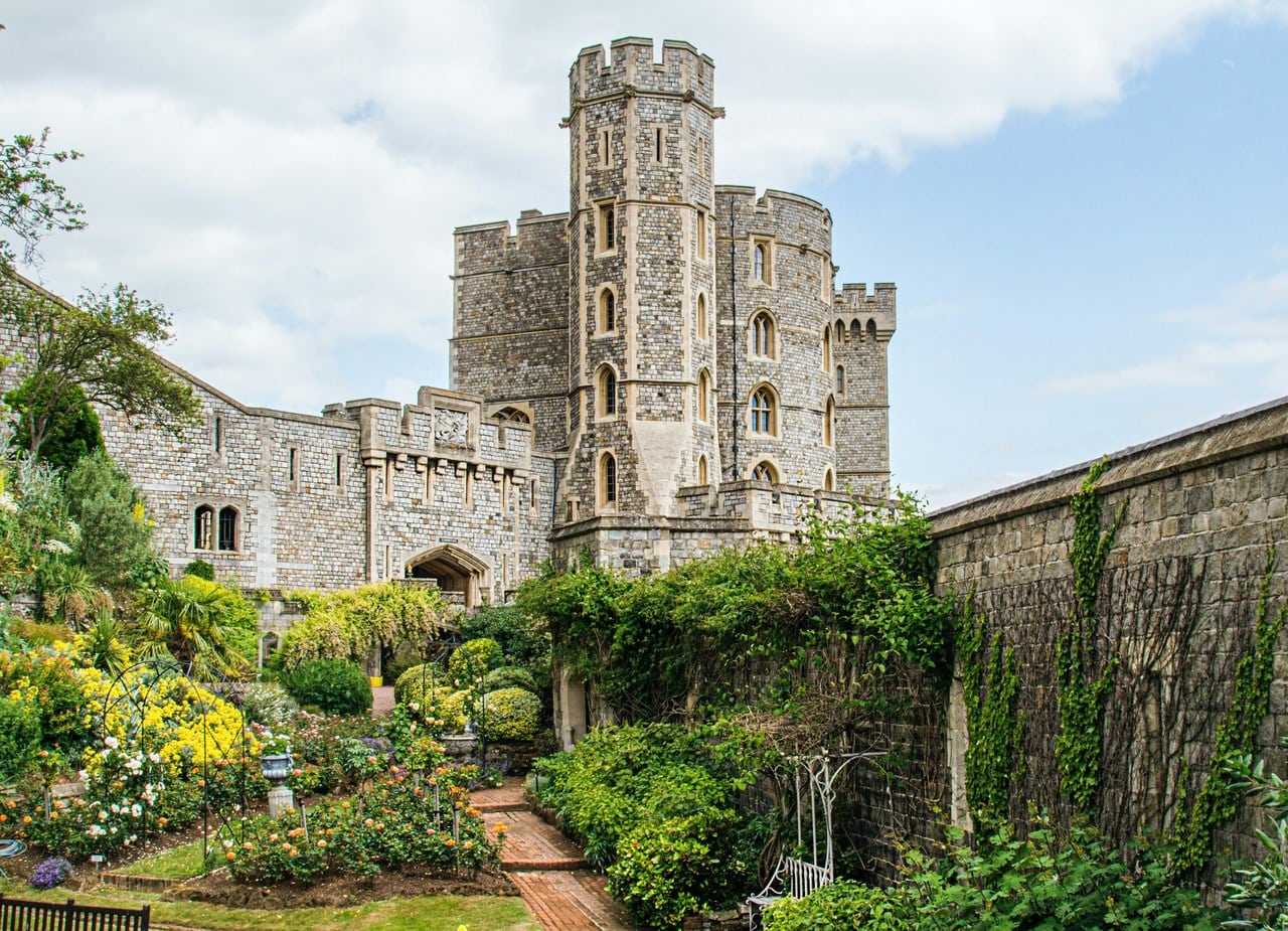 A sloping garden of roses and creeper-covered walls at the foot of a tall stone tower with a projecting stair turret, a high wall along one side A sloping garden of roses and creeper-covered walls at the foot of a tall stone tower with a projecting stair turret, a high wall along one side