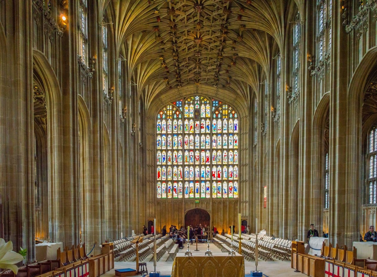 The interior of a tall Gothic chapel looking toward an immense stained-glass window, the ribbed vault spreading overhead above rows of seating The interior of a tall Gothic chapel looking toward an immense stained-glass window, the ribbed vault spreading overhead above rows of seating