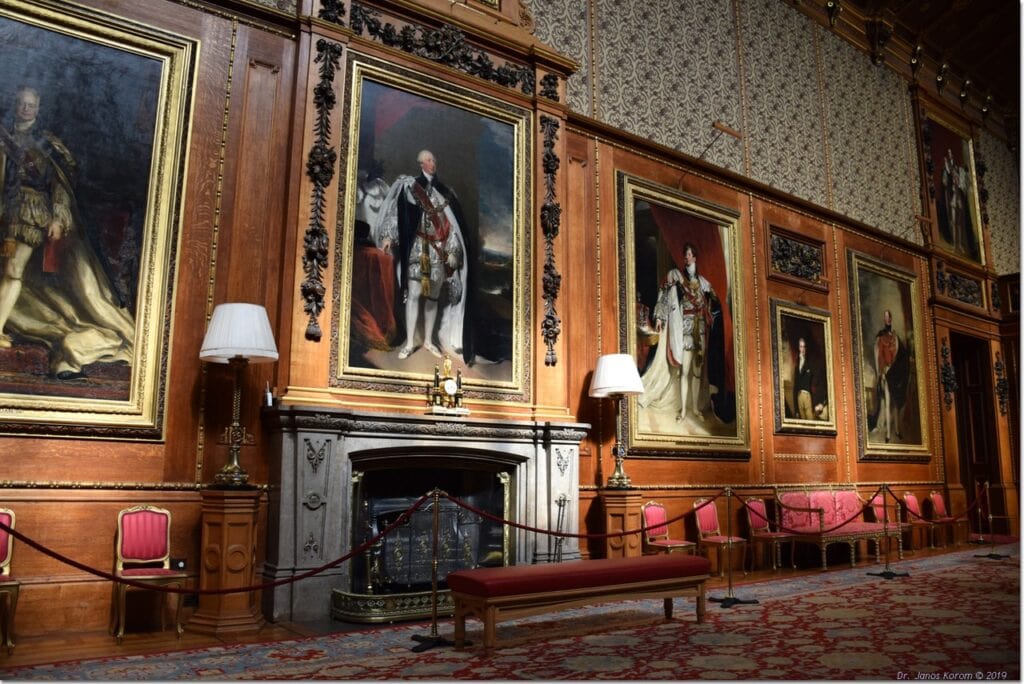 Windsor Castle 14 A tall room lined with large gilt-framed full-length portraits above wood panelling, with a chimneypiece and long benches down one side