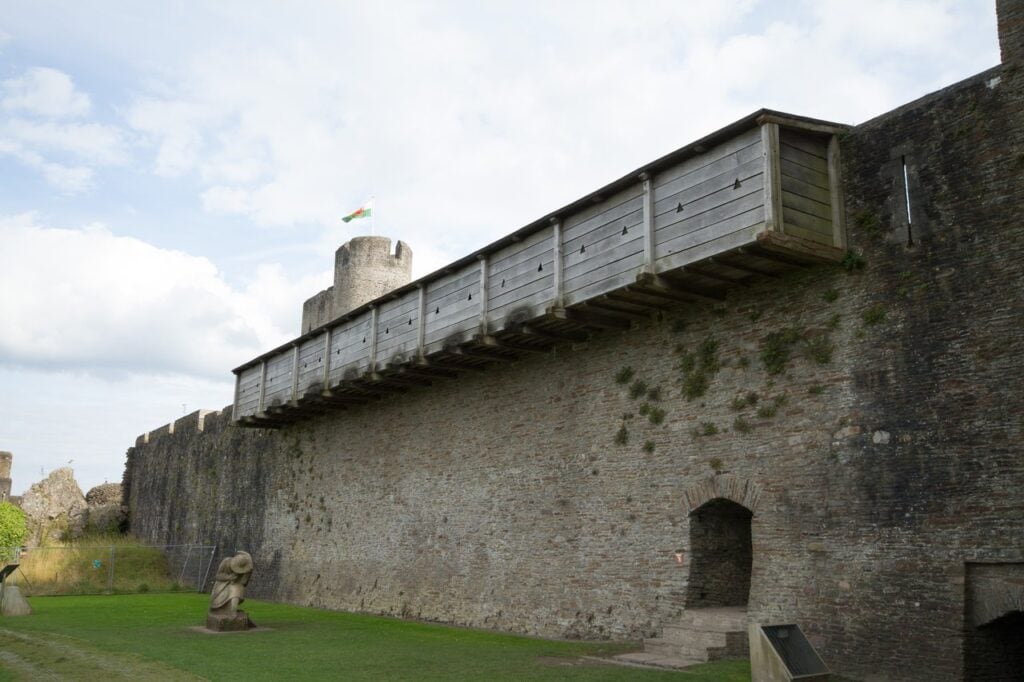 Caerphilly Castle 9 A covered timber gallery cantilevered out from the top of a stone curtain wall, seen from the grass below