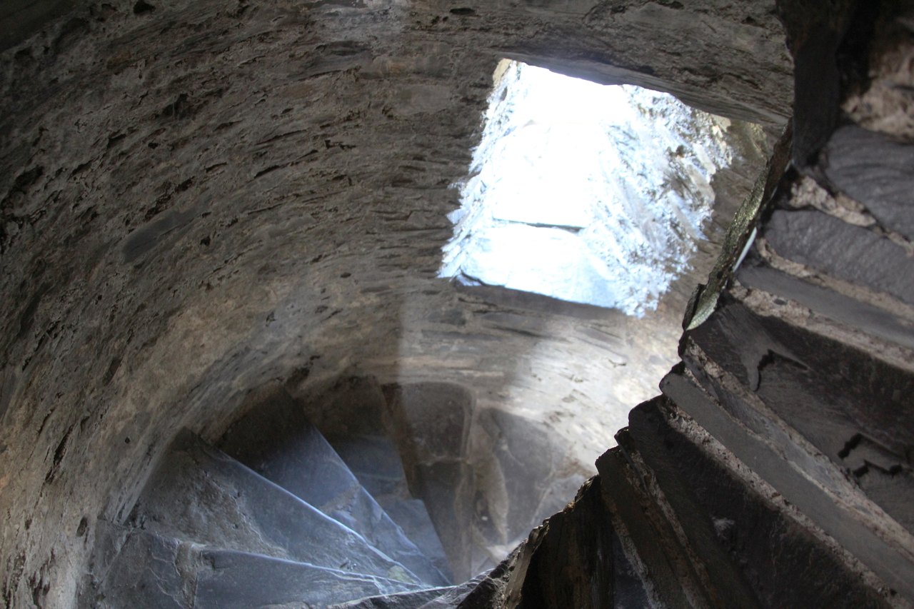 Worn slate steps of a narrow spiral staircase curving inside thick stone walls, lit from a bright opening above Worn slate steps of a narrow spiral staircase curving inside thick stone walls, lit from a bright opening above
