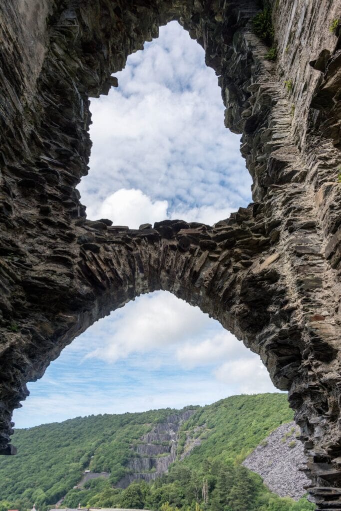 Dolbadarn Castle 7 Looking out from inside a stone tower through a pointed arched doorway, with a larger pointed opening with broken sides above it, to a wooded hillside scarred by gray slate tips