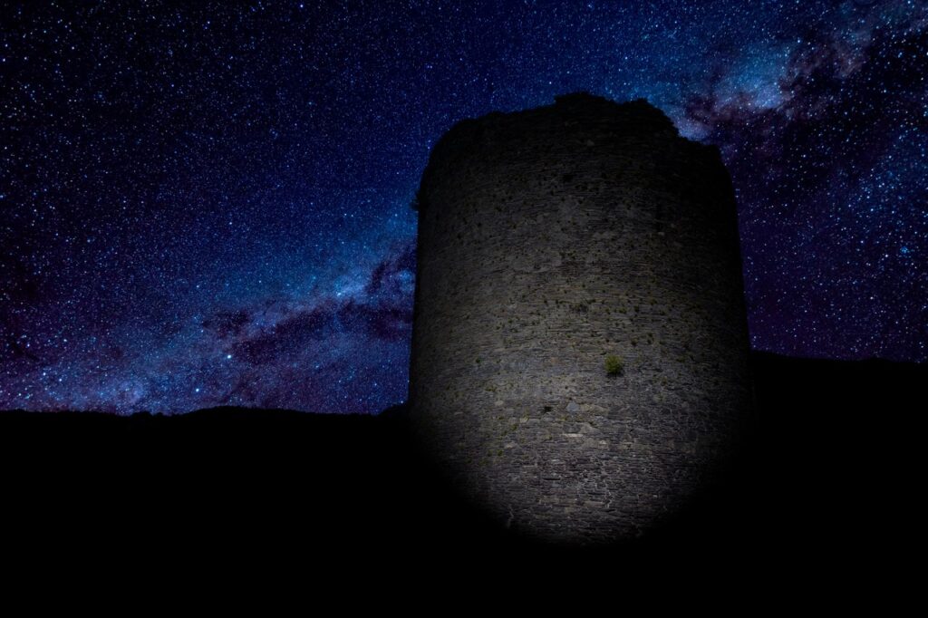 Dolbadarn Castle 14 A round stone tower lit from below at night, silhouetted against a star-filled sky with the band of the Milky Way